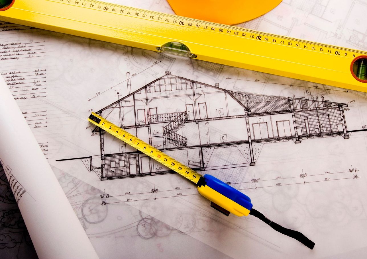 Schizzo architettonico con strumenti di misurazione gialli e matita da disegno su un foglio da progetto.