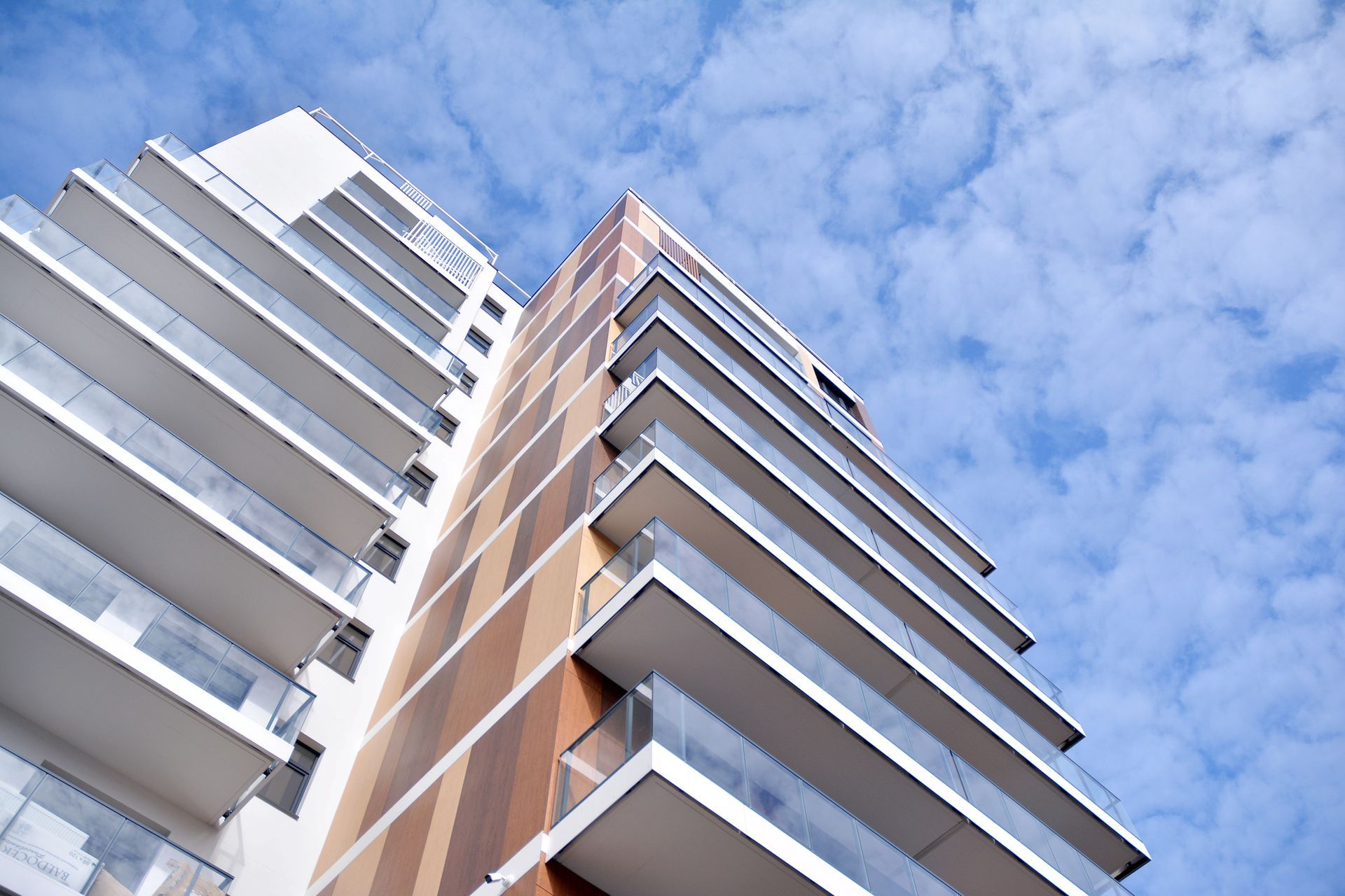 Vista dal basso di due moderne torri residenziali con balconi bianchi sullo sfondo di un cielo azzurro.