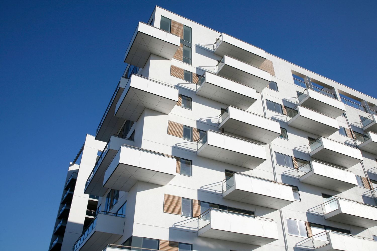Moderno palazzo residenziale bianco con balconi che si stagliano contro un cielo azzurro limpido.