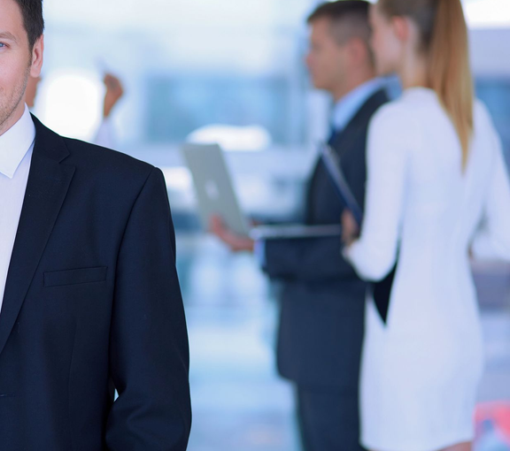 Professionisti in giacca e cravatta che conversano in un luminoso corridoio d'ufficio.