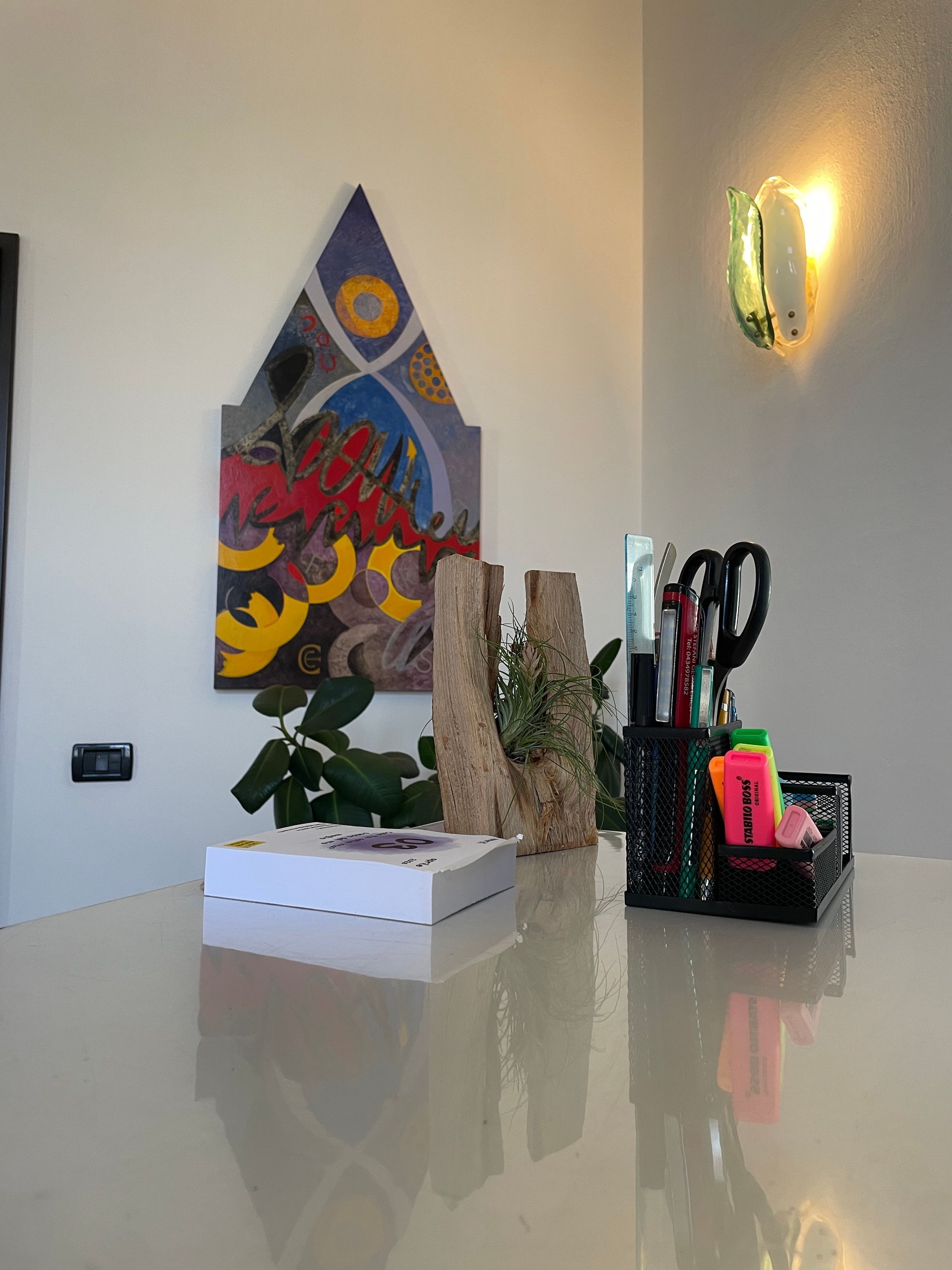 Quadri decorativi, piante e utensili da cucina su un bancone in una stanza luminosa.