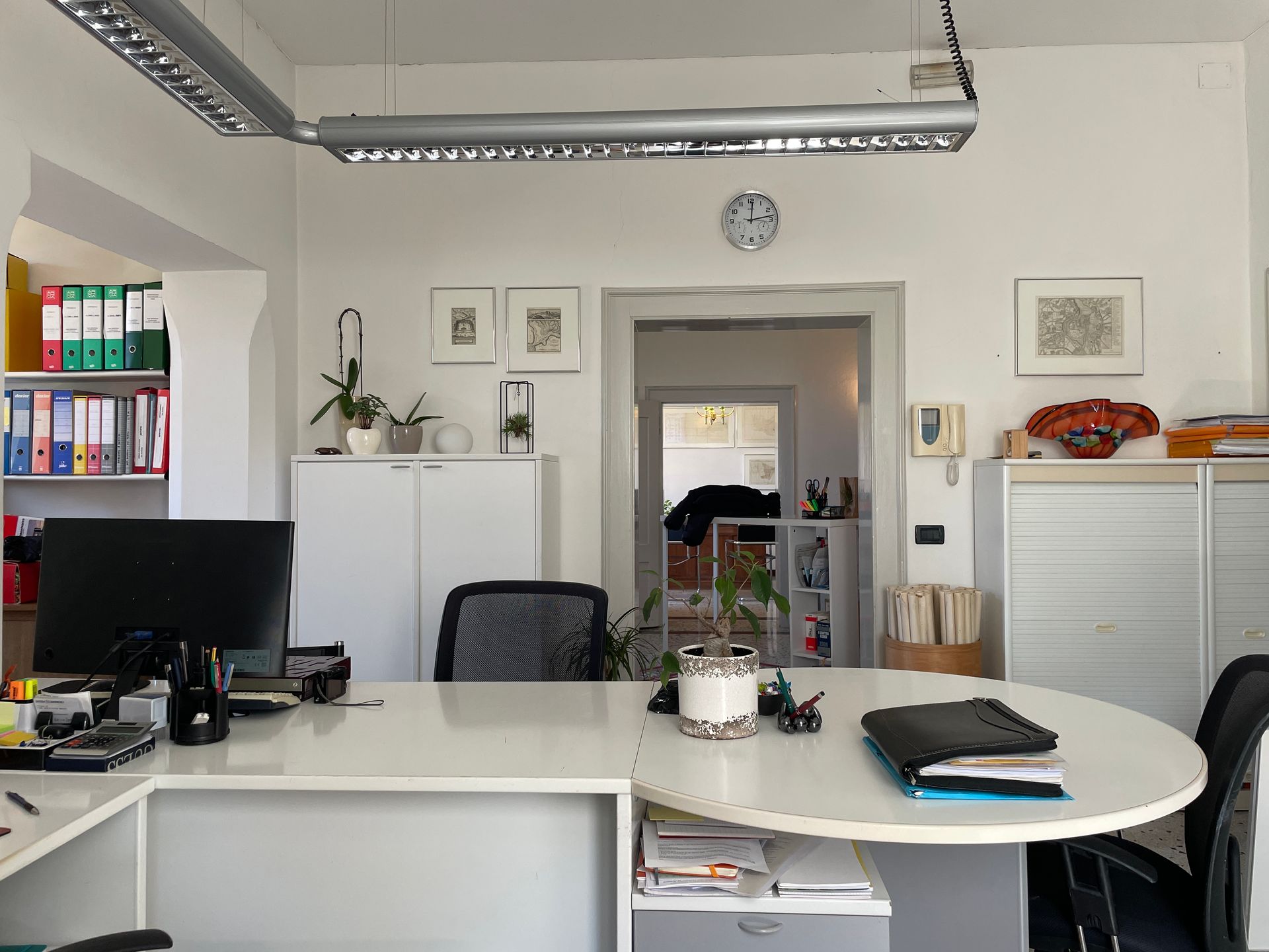 Luminosa area reception con scrivanie, computer, armadietti bianchi e quadri appesi alle pareti.