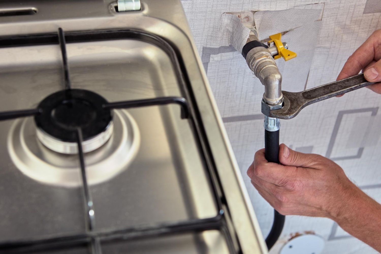 A person is fixing a gas hose on a stove with a wrench.