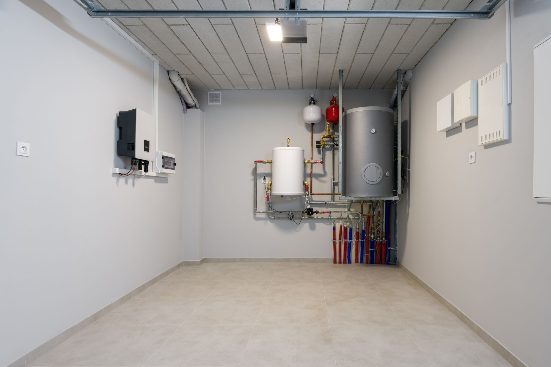 Empty utility room with boilers, tanks, and exposed piping along a white wall