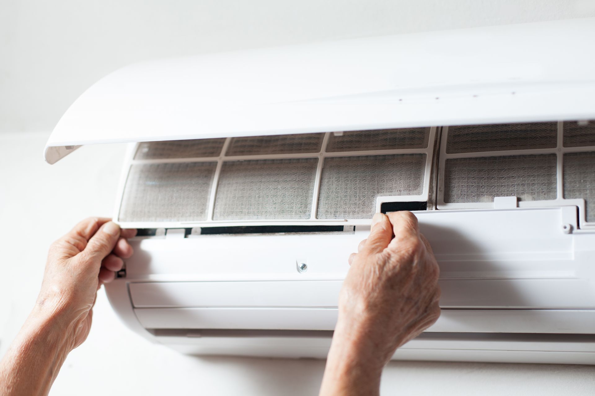 Hands removing a dirty air conditioner filter from a white unit.
