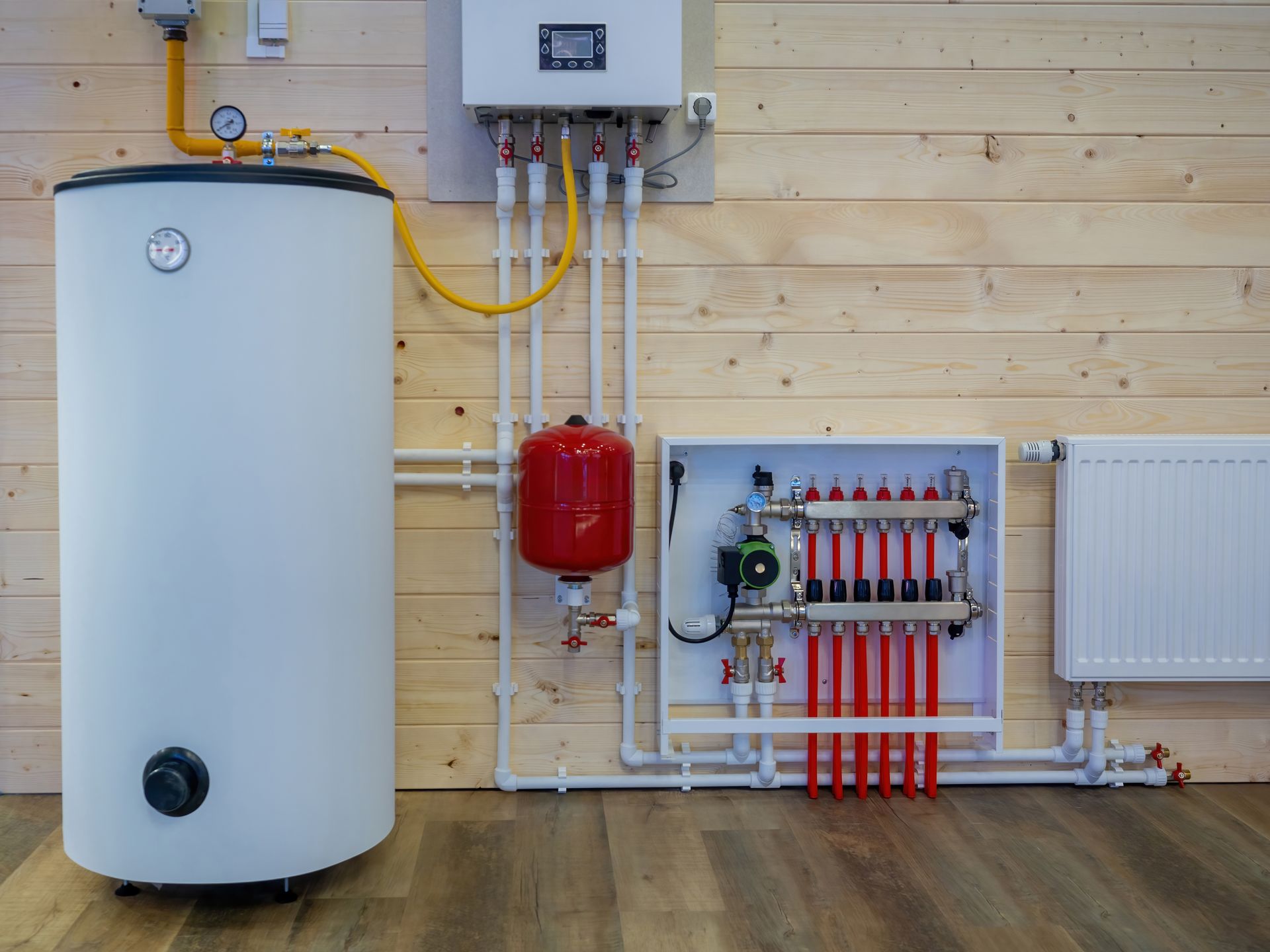 Wall-mounted heating system with white tank, red expansion tank, boiler, and manifold against wood paneling