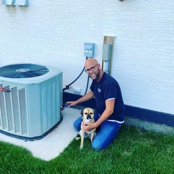 A man is kneeling next to a dog in front of an air conditioner