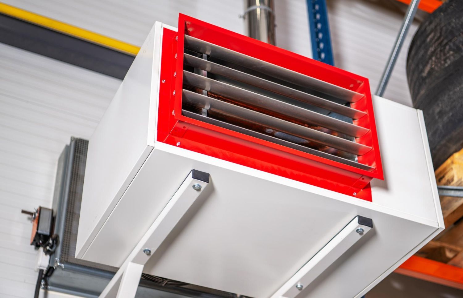 White and red industrial heater mounted on a metal bracket in a warehouse.