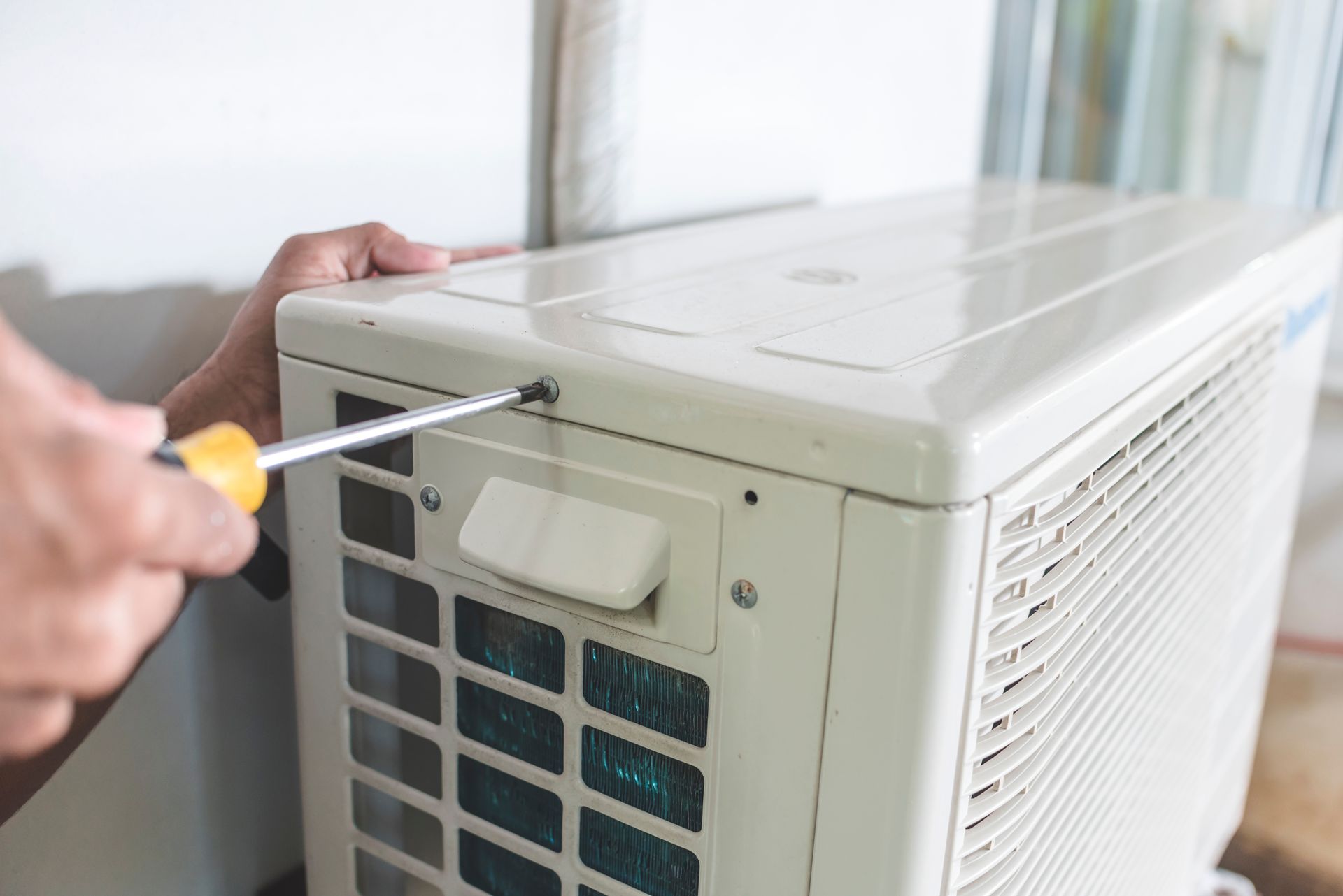 Hand using a screwdriver to open the side panel of a white air conditioner unit