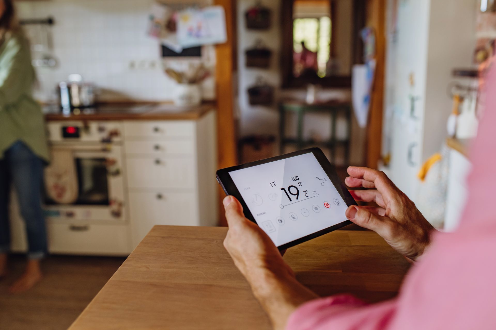 Person holding a tablet at a kitchen table, with a bright kitchen in the background