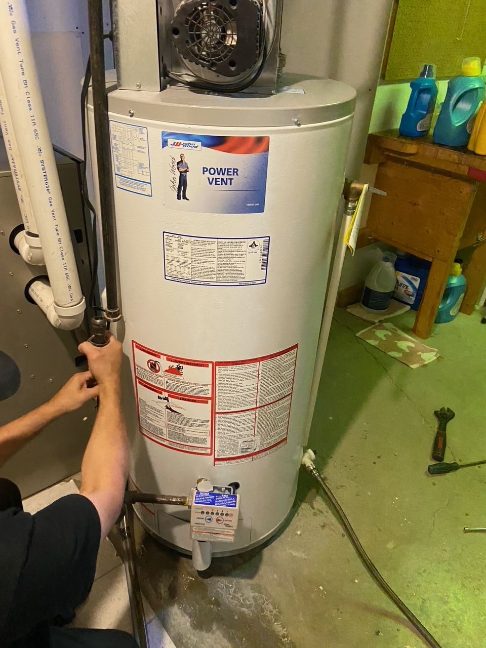 A man is working on a water heater in a basement.