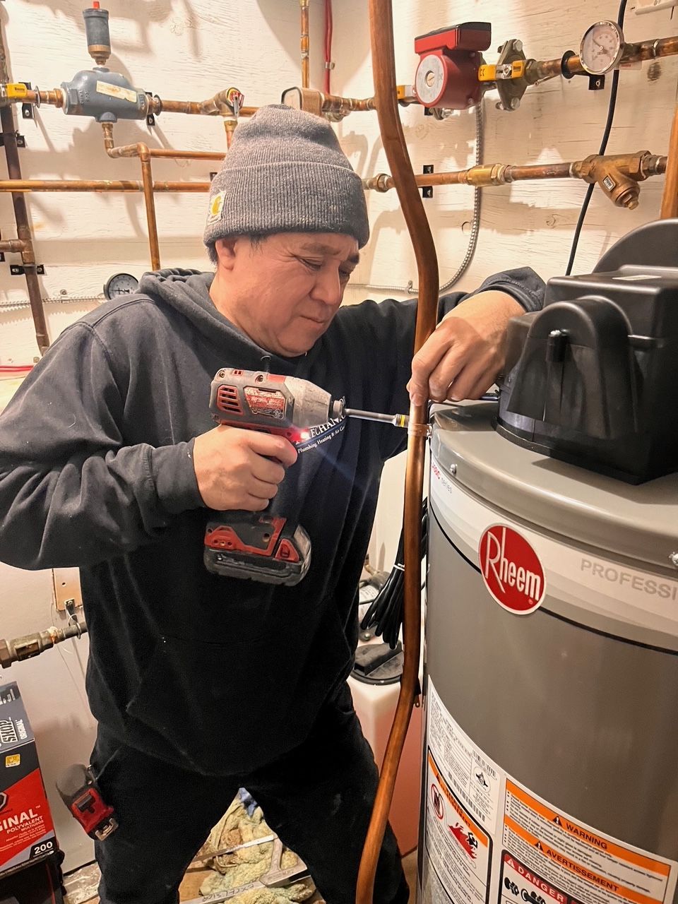 A man is using a drill to fix a water heater.