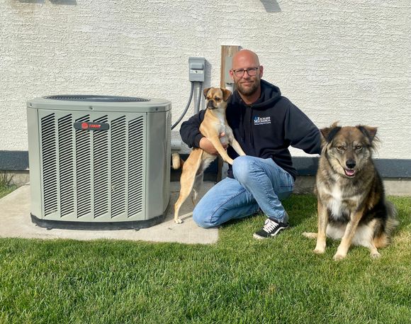 a man is kneeling down with two dogs in front of an air conditioner .
