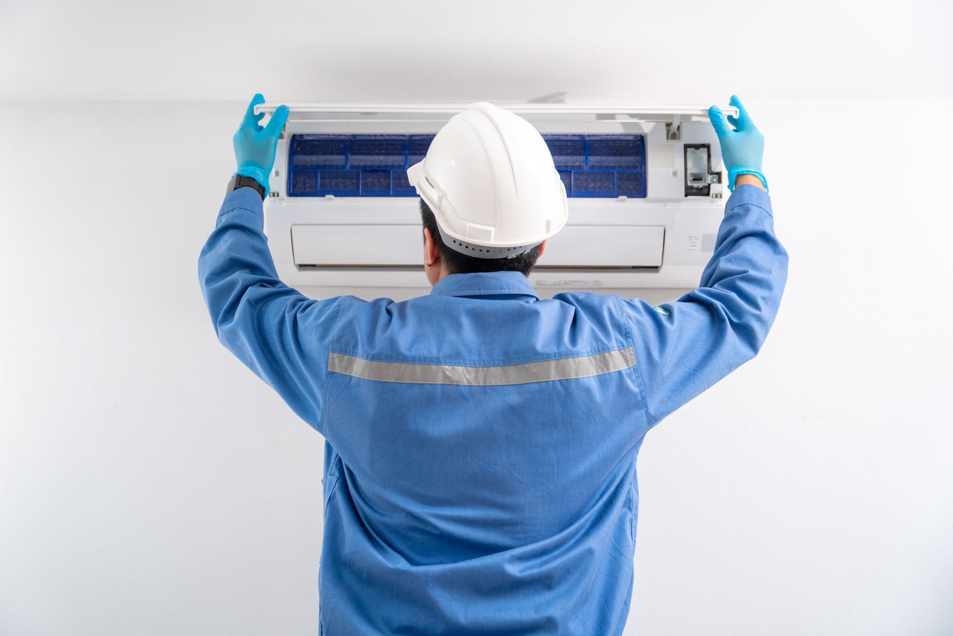 a man wearing a hard hat and gloves is installing an air conditioner .