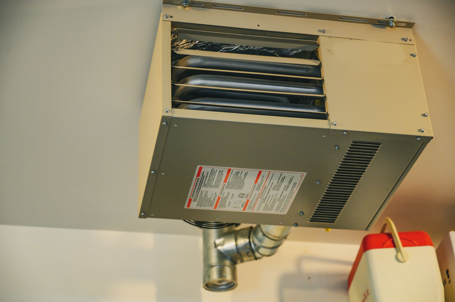 A heater is hanging from the ceiling next to a pipe.