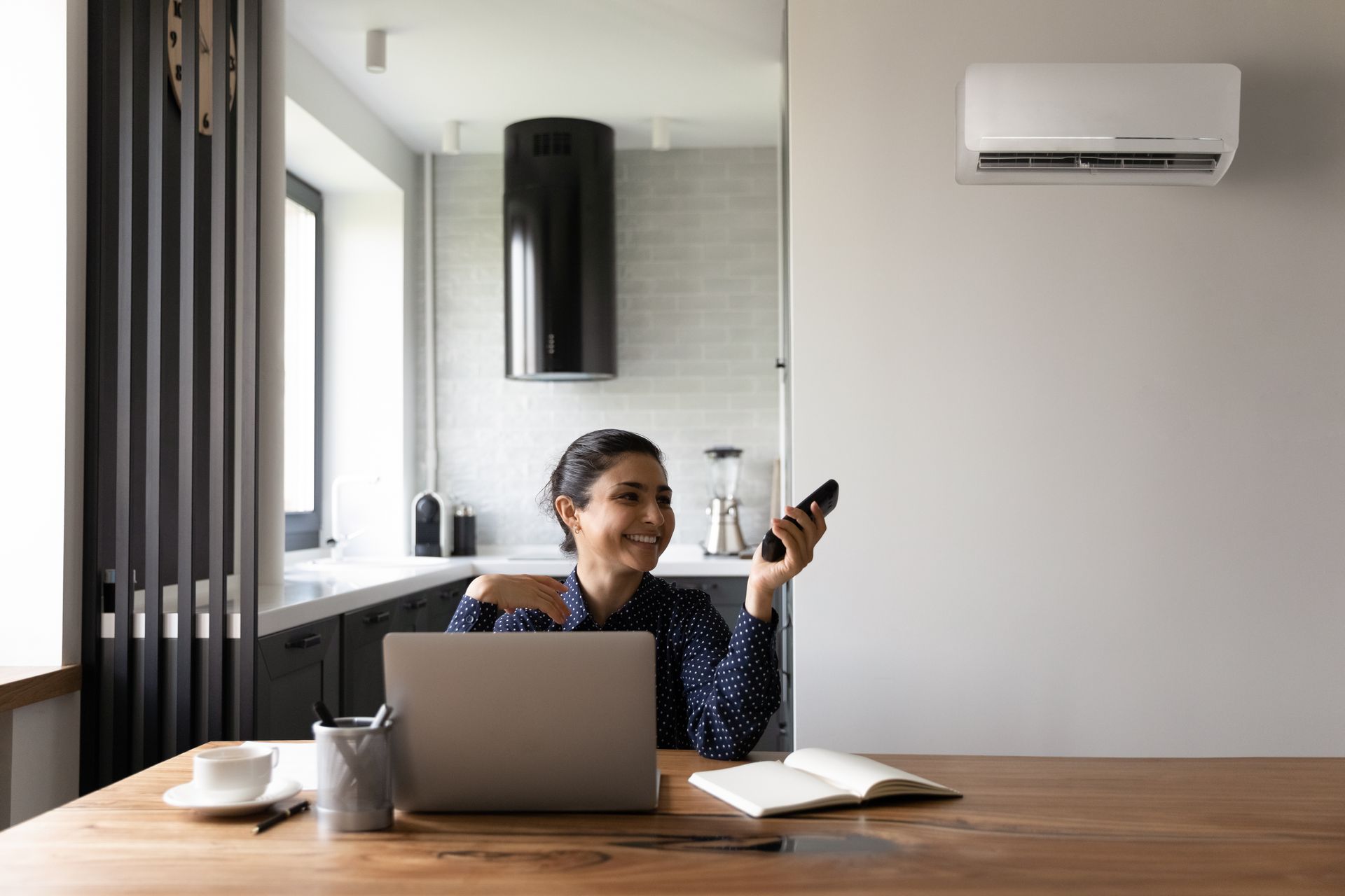 a woman is sitting at a table with a laptop and a remote control .