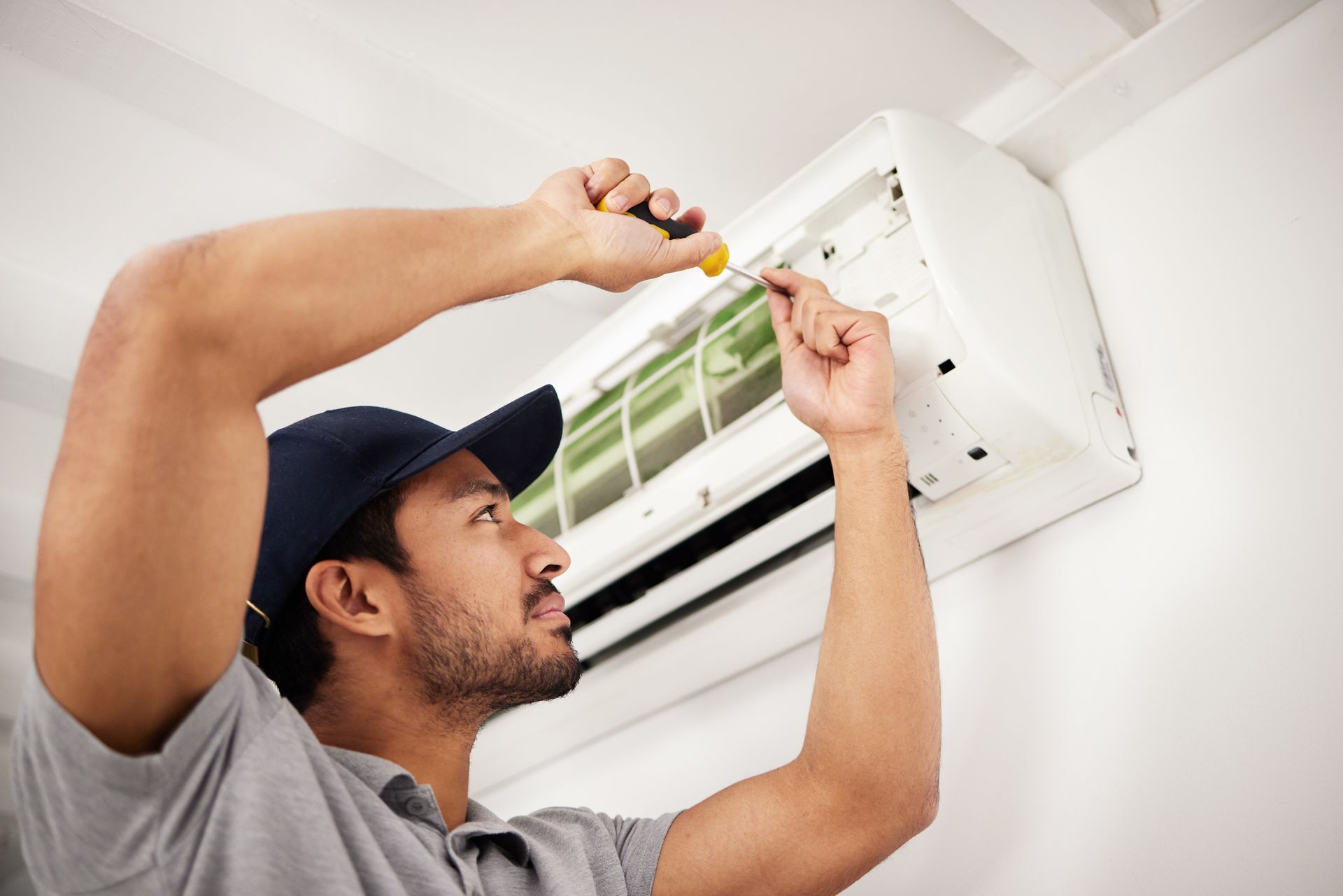 A man is fixing an air conditioner with a screwdriver.