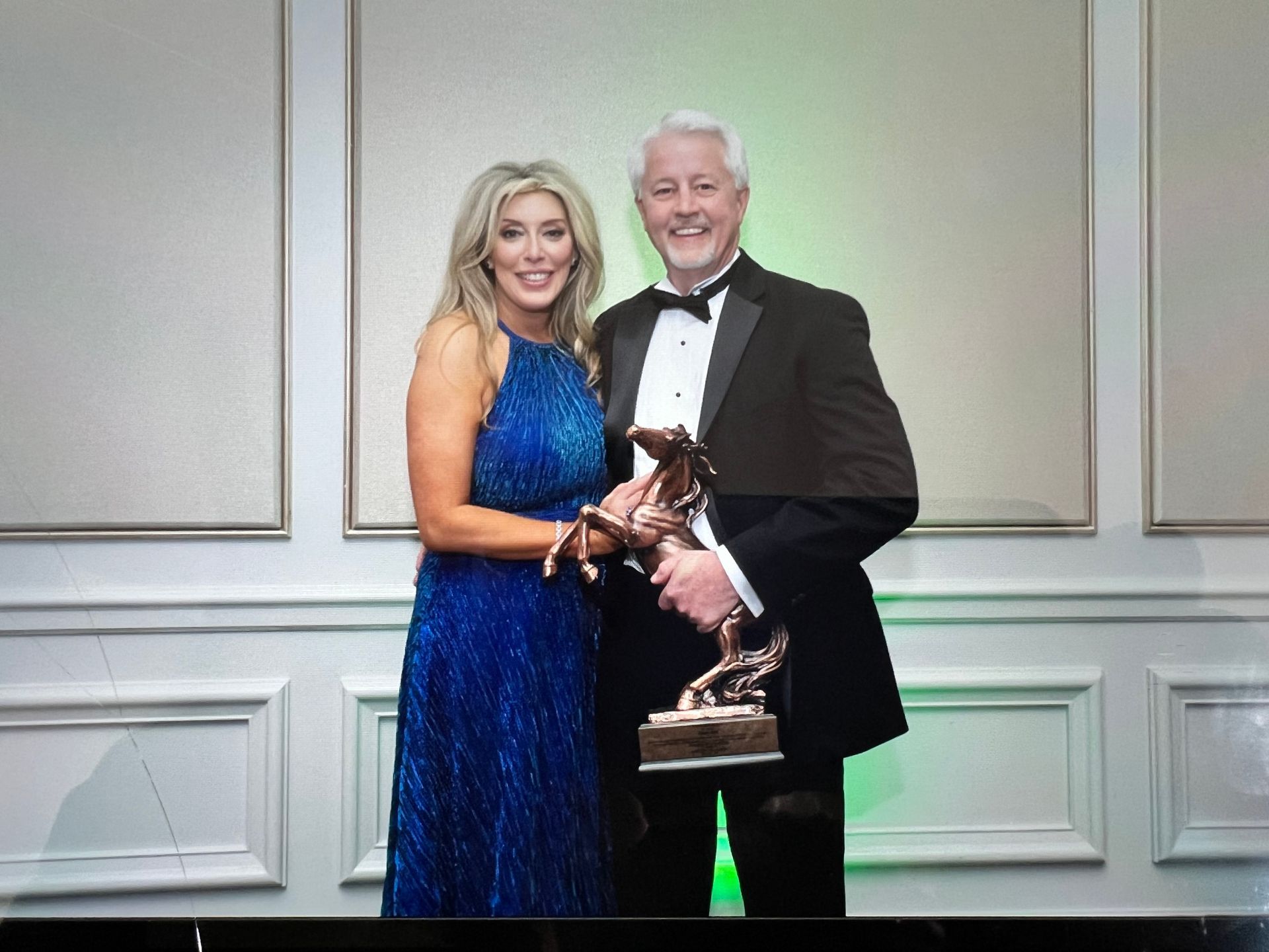 A man in a tuxedo is holding a trophy next to a woman in a blue dress