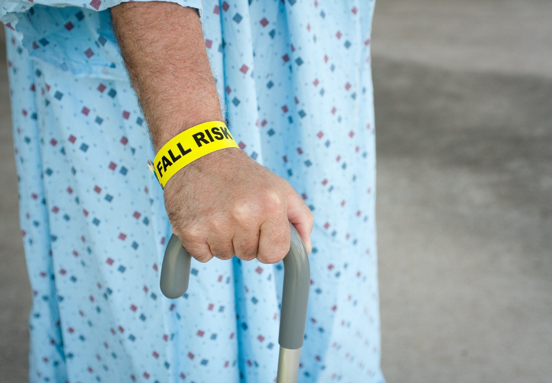 An elderly woman wearing a yellow wristband that says `` fall risk '' is holding a cane.