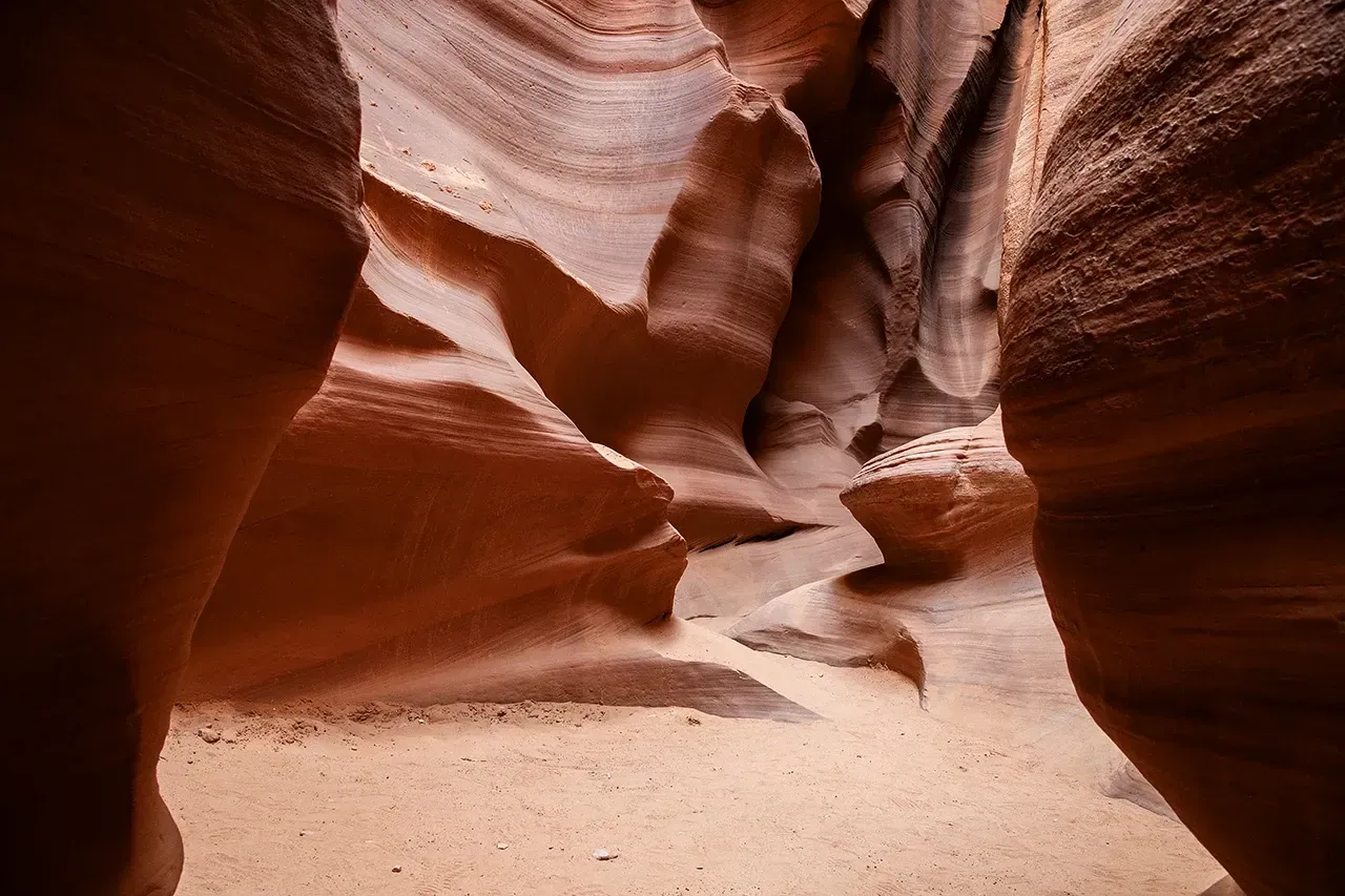 Narrow red sandstone slot canyon with a sandy floor and curved rock walls