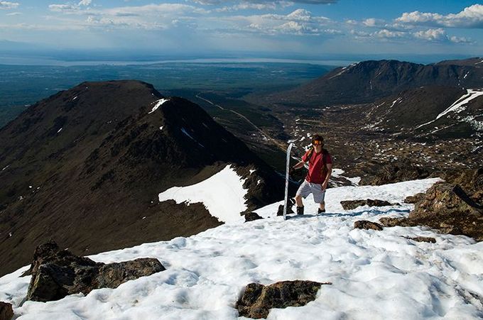 Hiker in red jacket standing on snowy mountain summit with rocky peaks and valley below