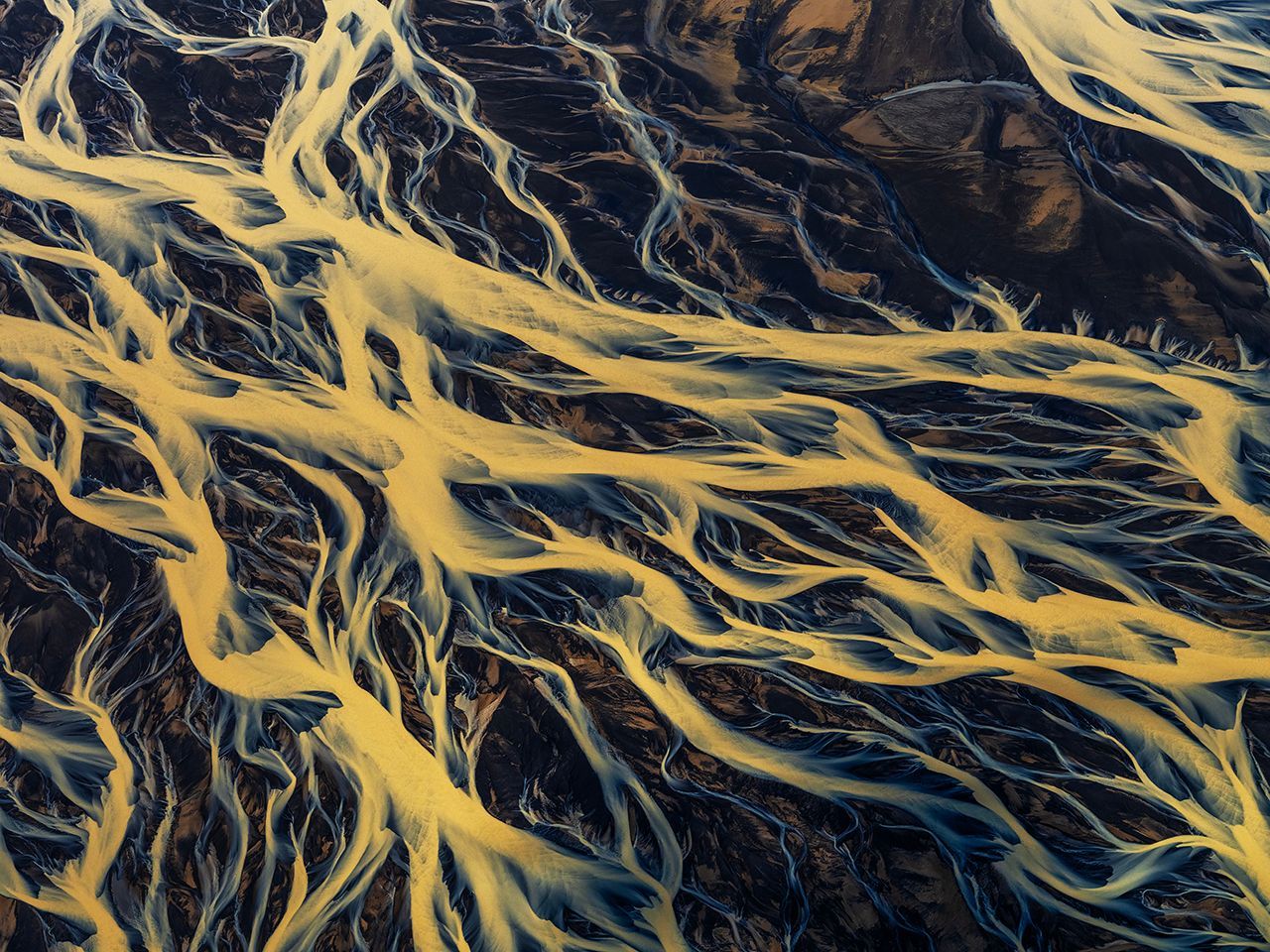 Aerial view of a dark river winding through bright yellow-green wetlands and rocky terrain.