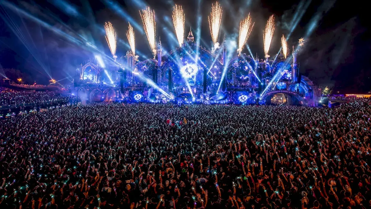 Night concert crowd facing a blue-lit stage with fireworks and bright pyrotechnics overhead