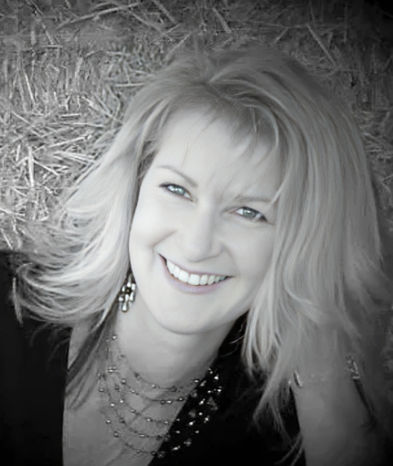 A woman is smiling in front of a pile of hay
