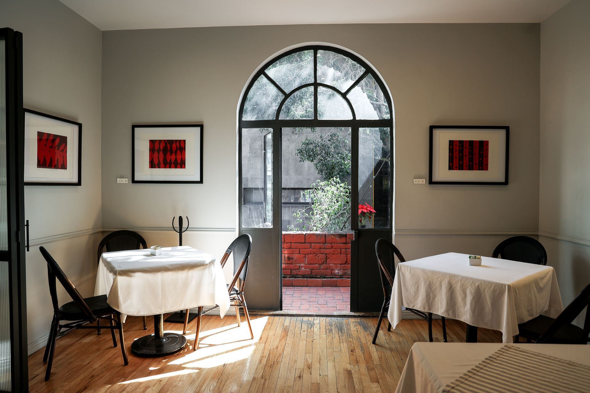 Pequeño comedor con dos mesas, puertas de cristal arqueadas y vistas a un patio de ladrillo.