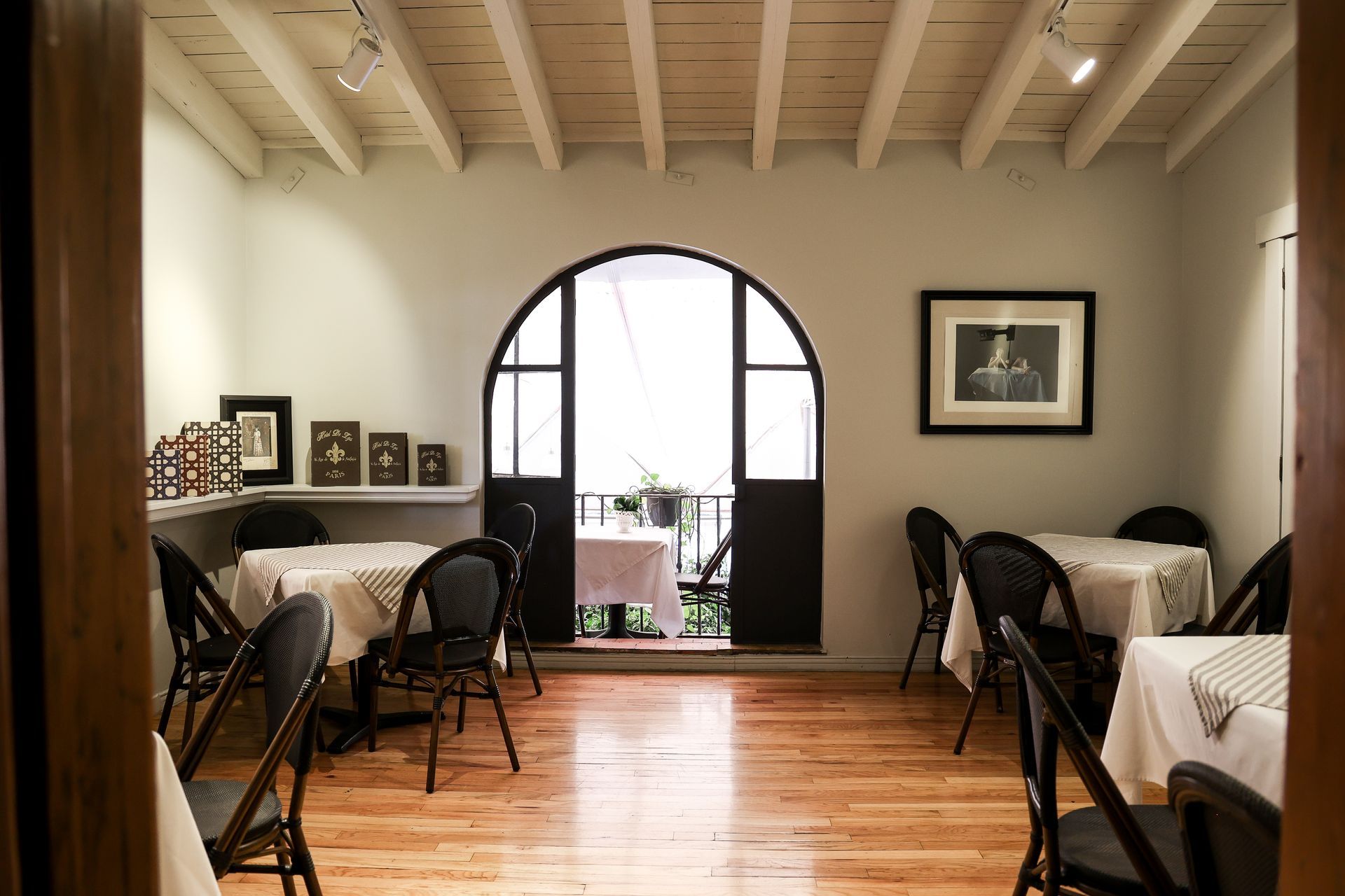 Comedor vacío con puerta arqueada, manteles blancos y cálidos suelos de madera.