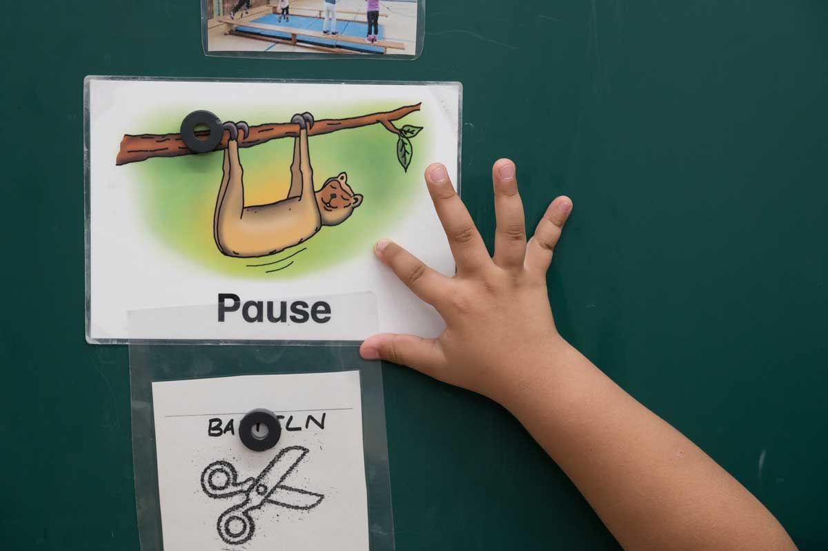 Eine Kinderhand zeigt auf ein Schild mit dem Wort „Pause“