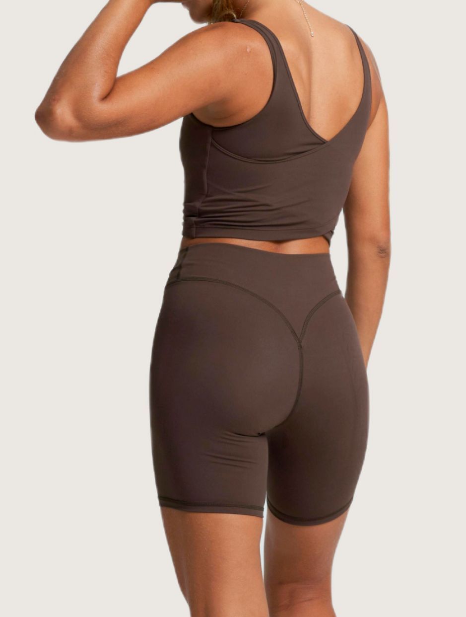 Woman in brown athletic wear, back view. Crop top, high-waisted shorts.