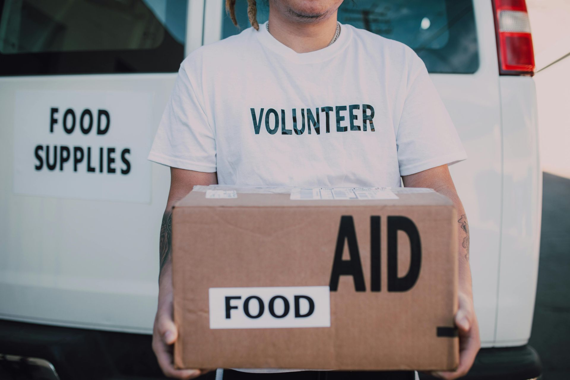 A volunteer is holding a box of food in front of a food supplies van.