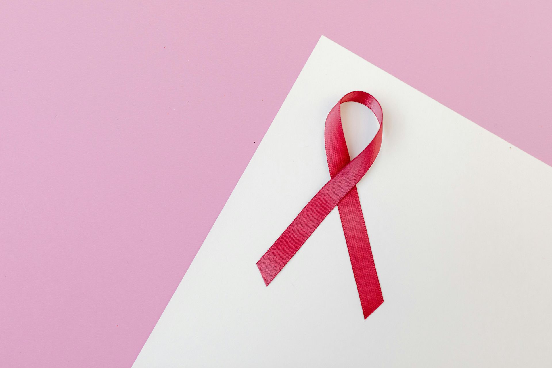 A red ribbon is on a piece of paper on a pink background.
