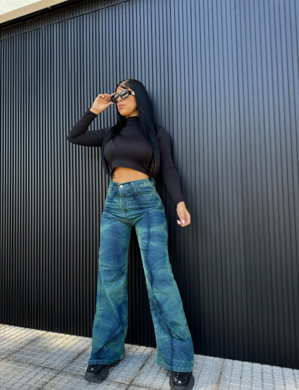 Una mujer que viste un top negro y jeans azules está parada frente a la puerta de un garaje.