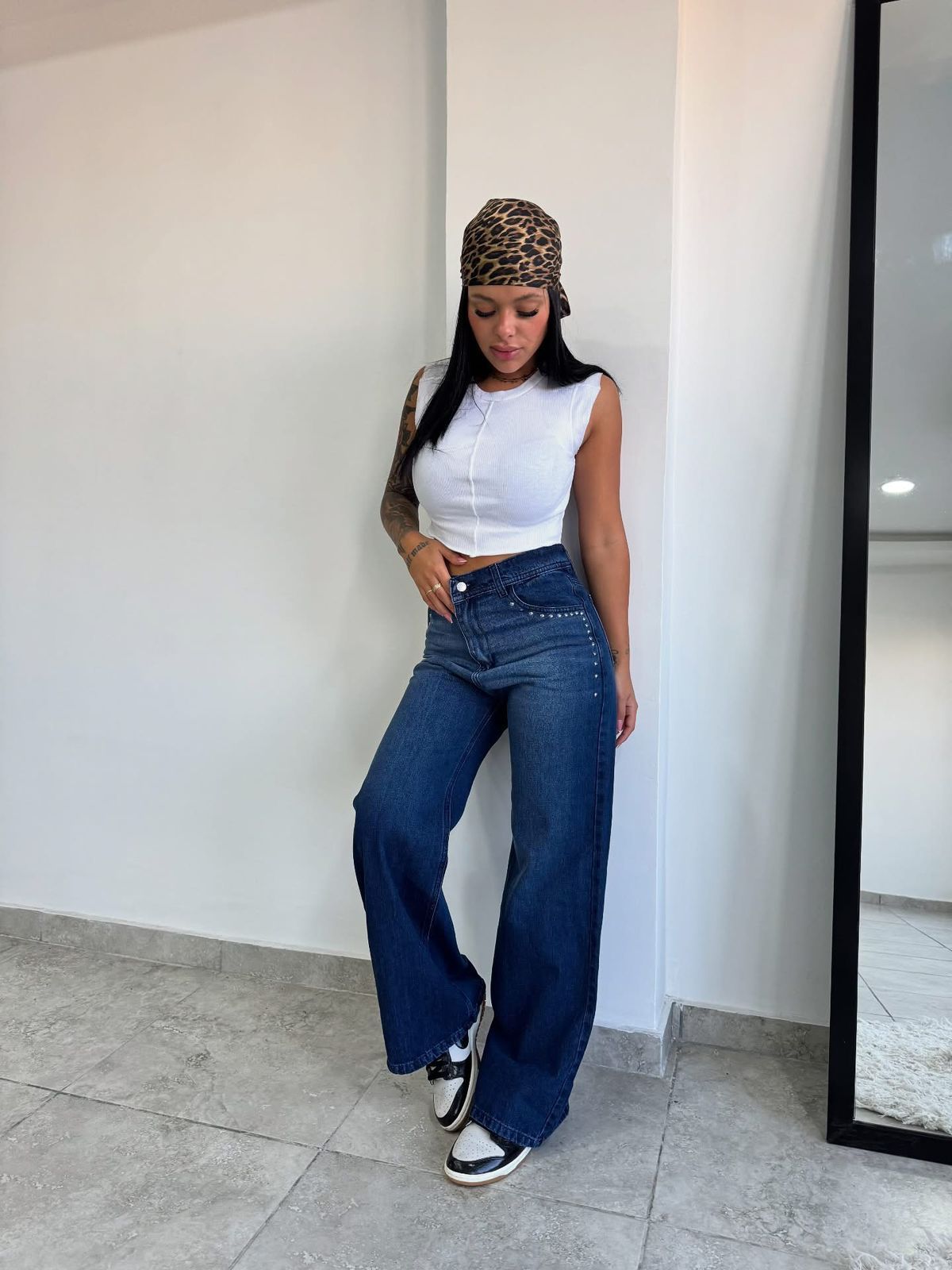 Una mujer que viste un top blanco y jeans de pierna ancha está parada frente a un espejo.