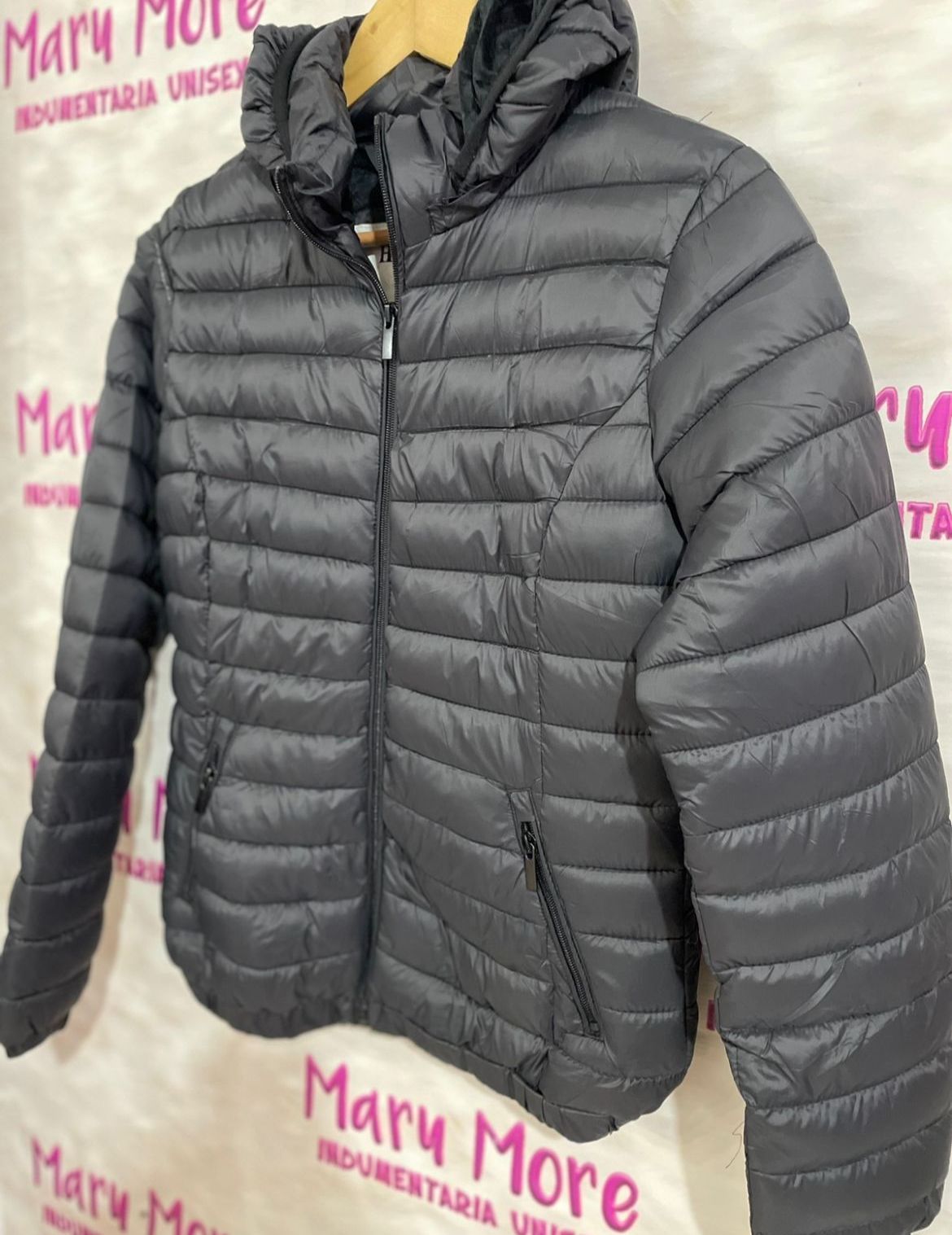 Una chaqueta negra está colgada en una percha delante de un cartel que dice Mary More.