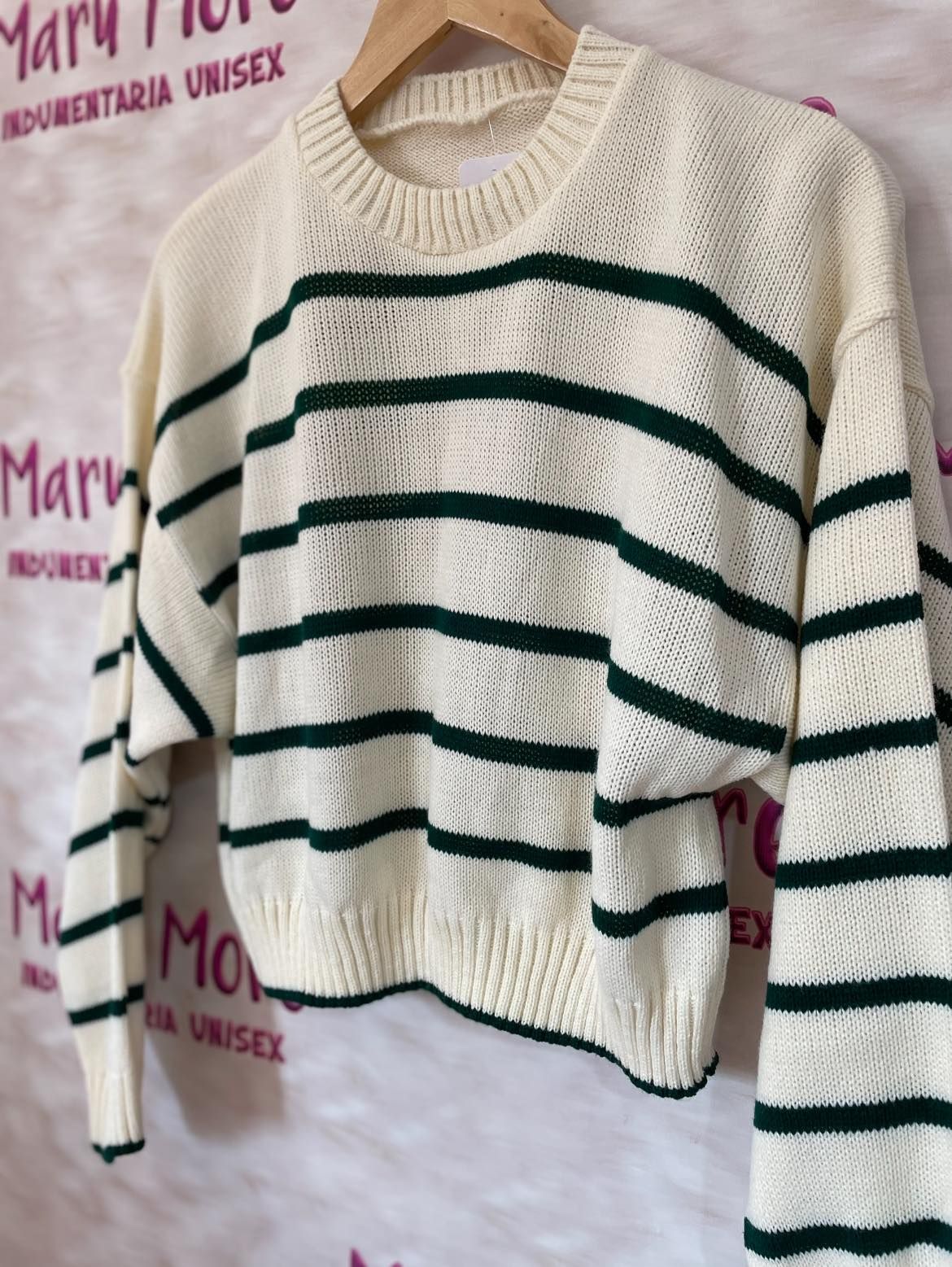 Un suéter de rayas blancas y verdes está colgado en una percha de madera.