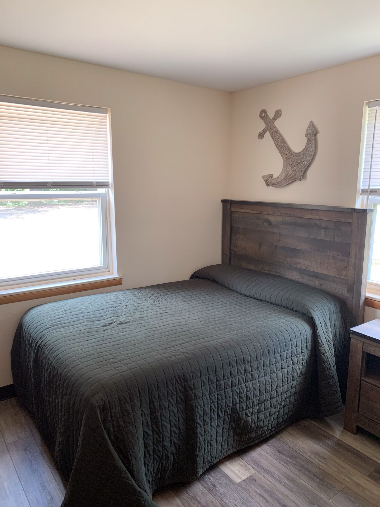 A bedroom with a bed , nightstand , window and anchor on the wall.