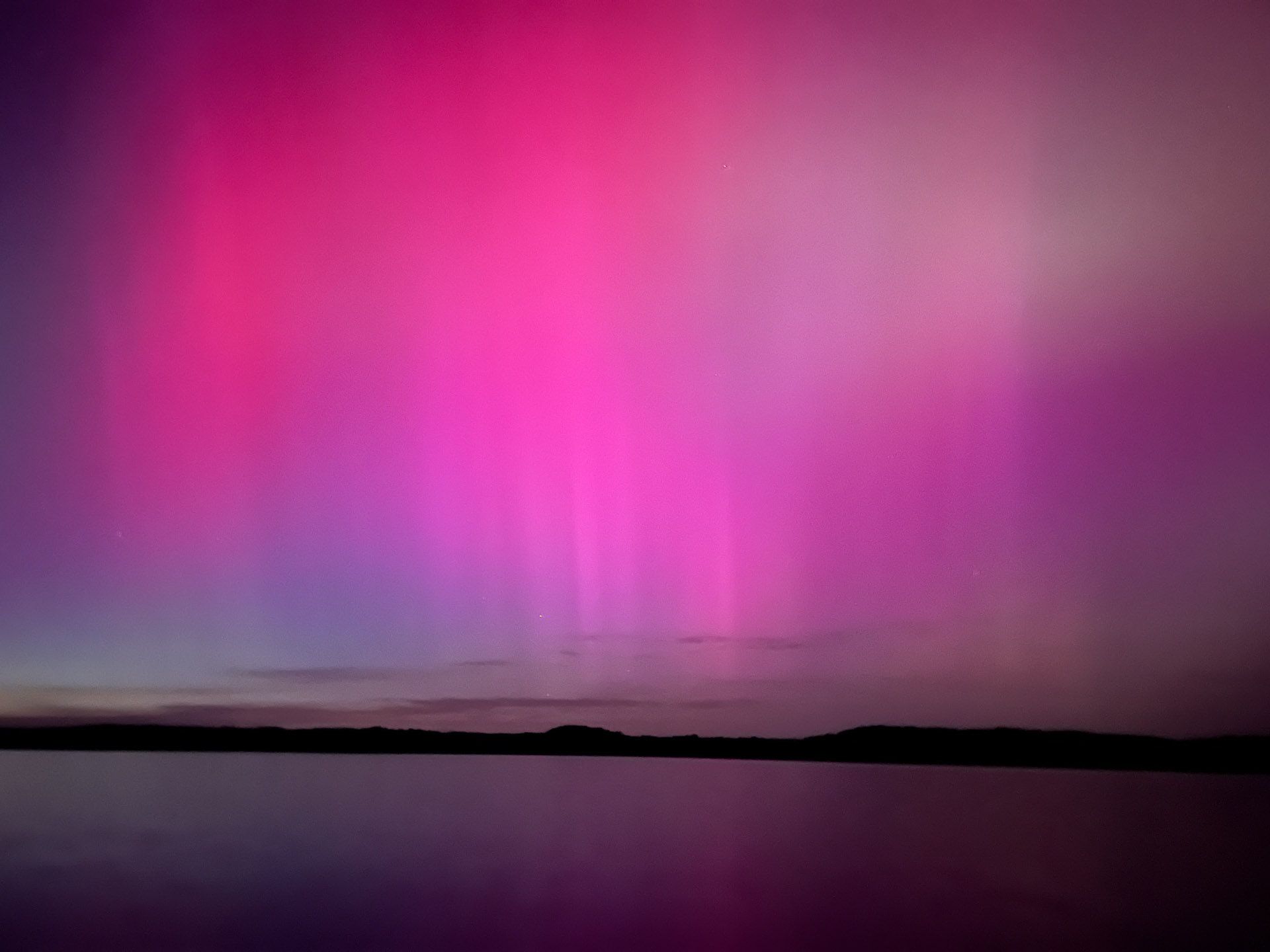 The aurora borealis is glowing in the night sky over a lake.