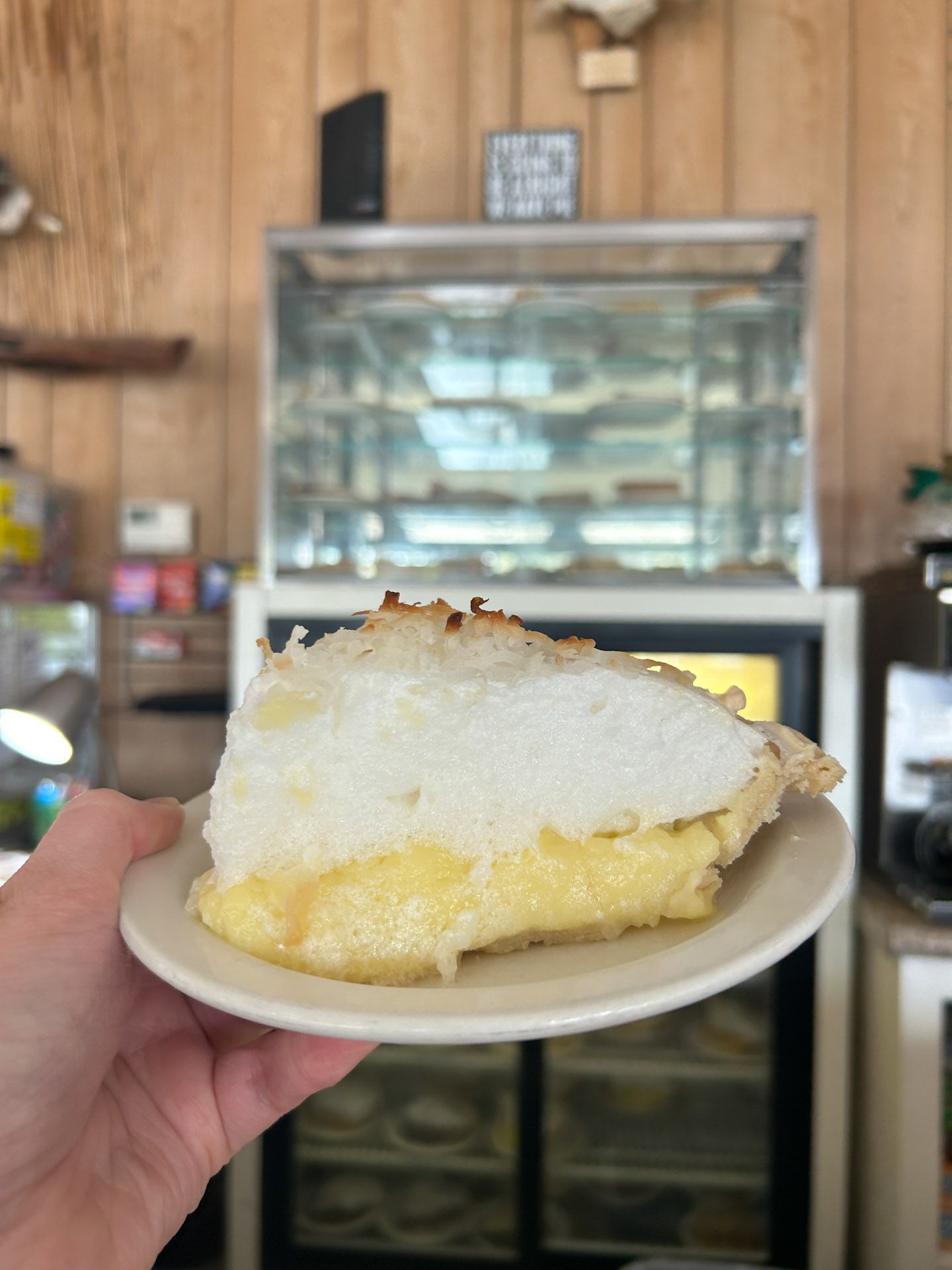 A person is holding a slice of lemon meringue pie on a plate.