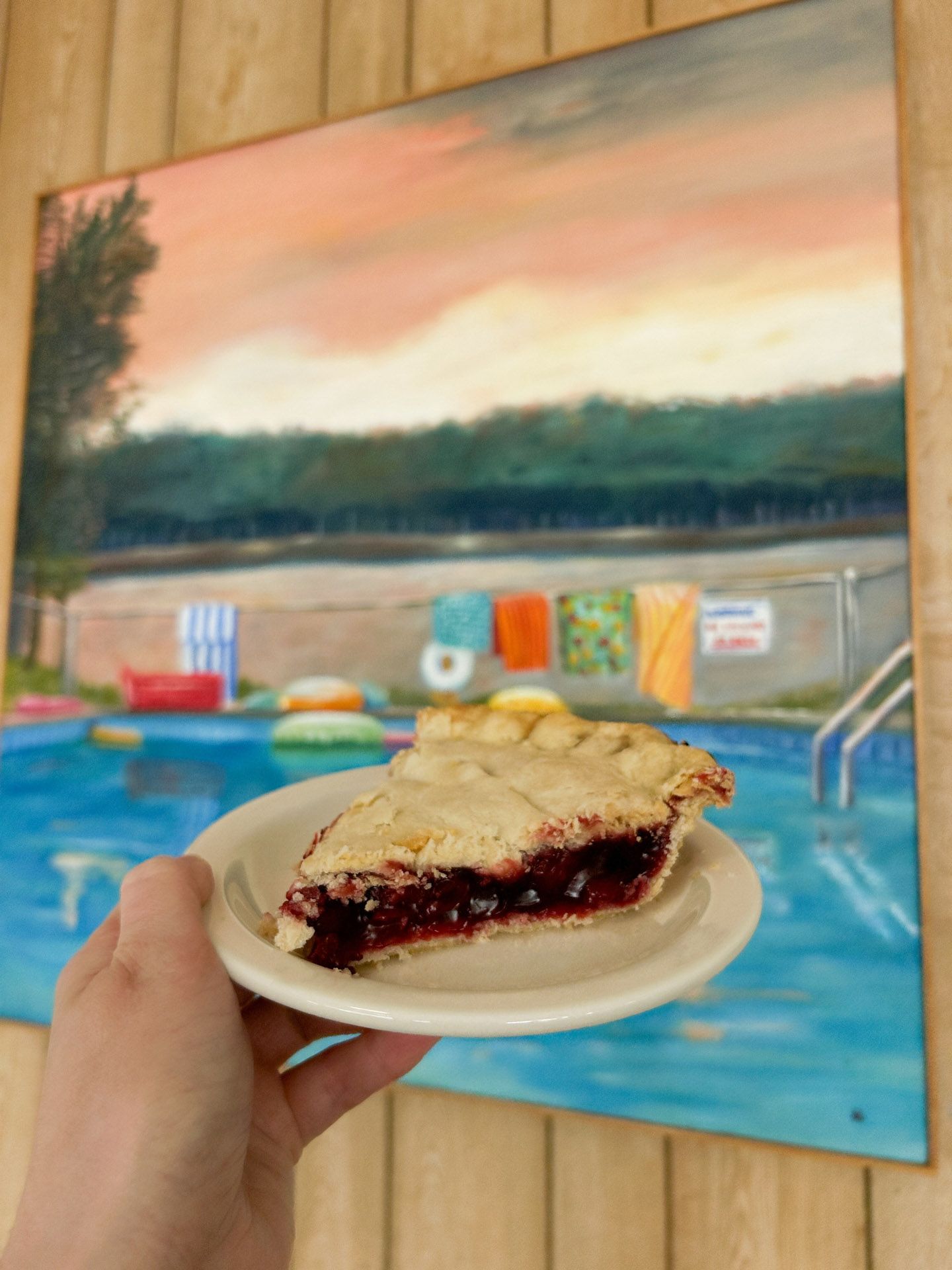 A person is holding a plate of pie in front of a painting of a pool