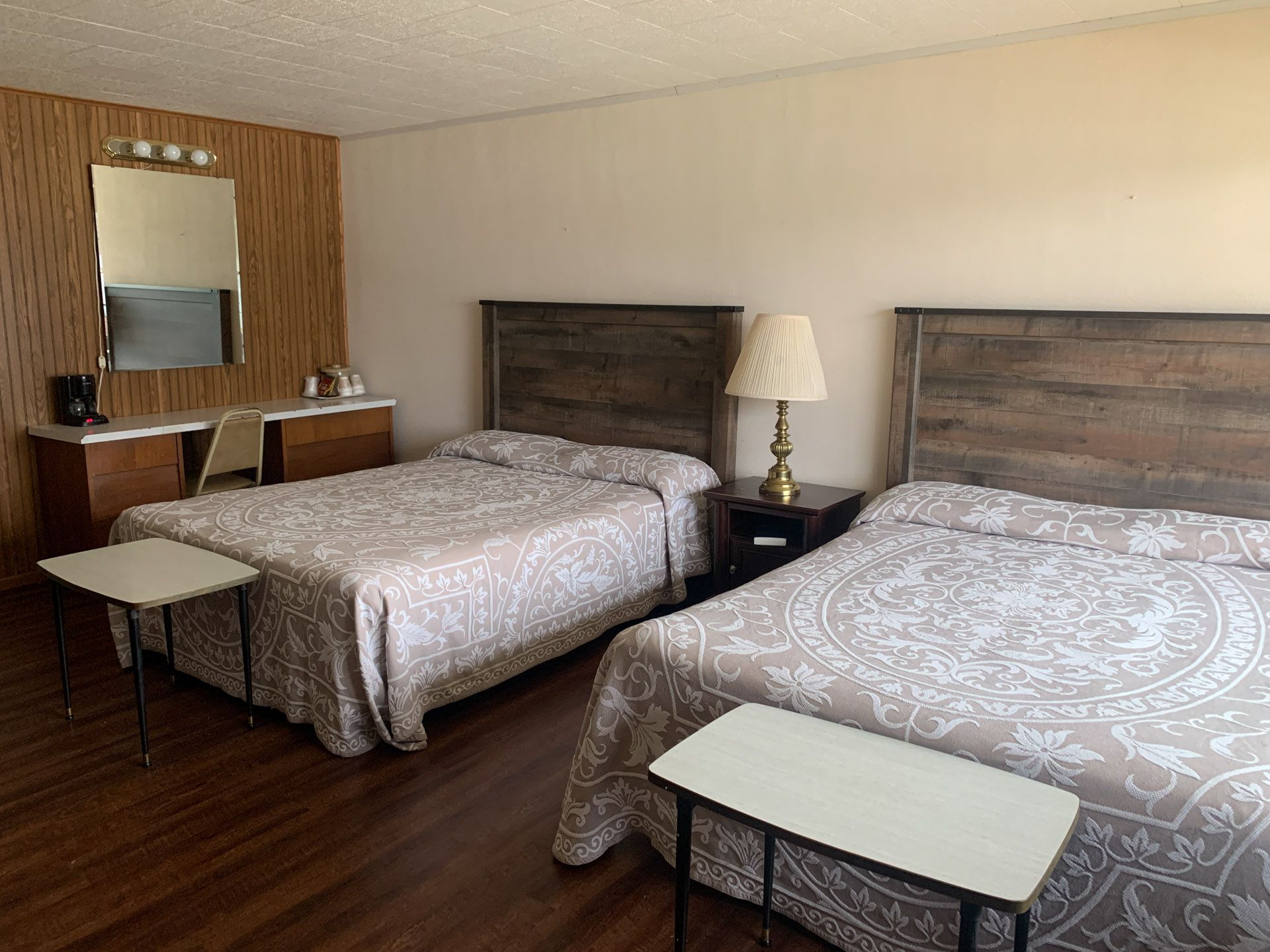 A hotel room with two beds , a desk , a lamp and a mirror.