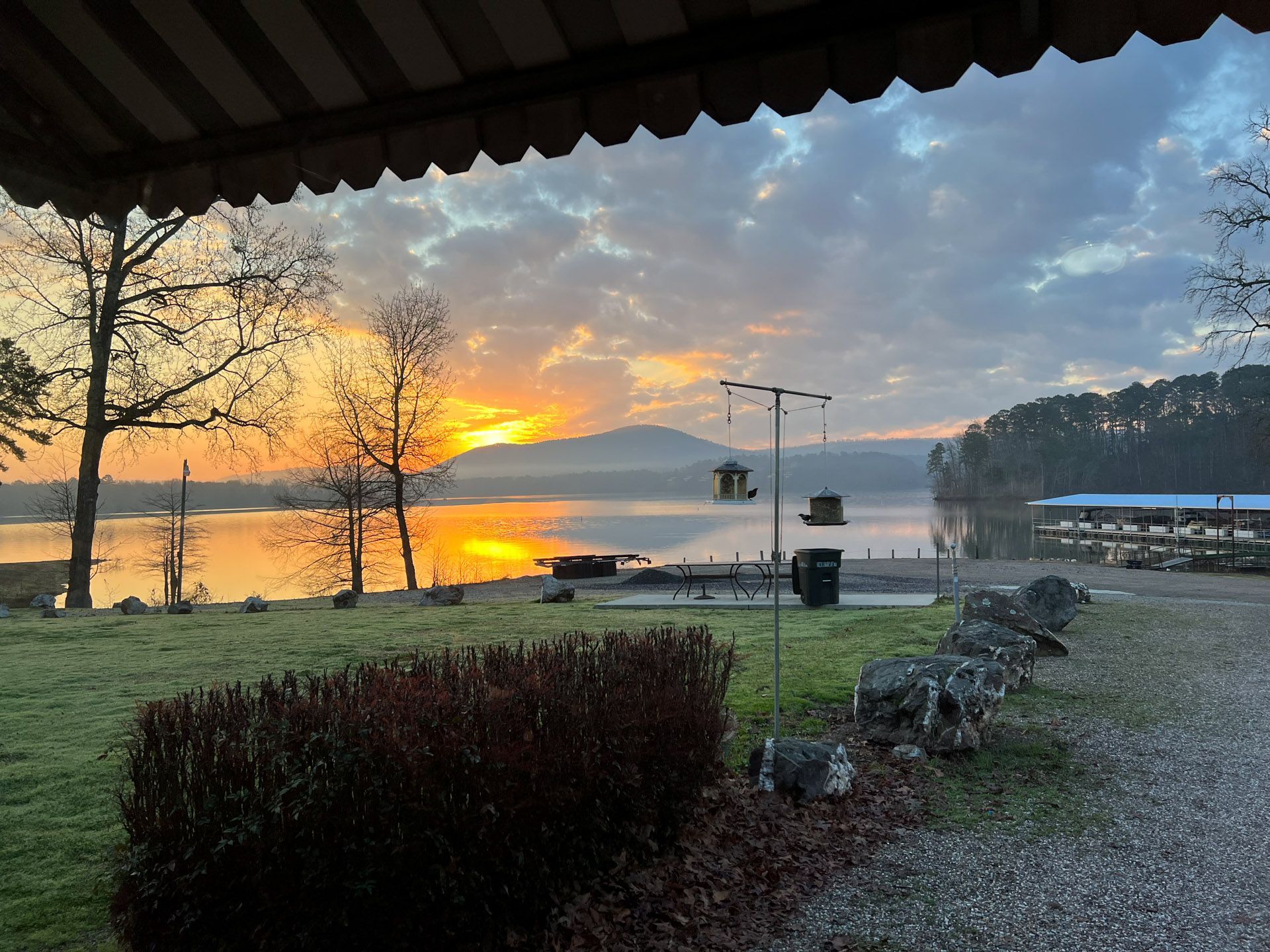 A sunset over a lake with a bird feeder in the foreground.