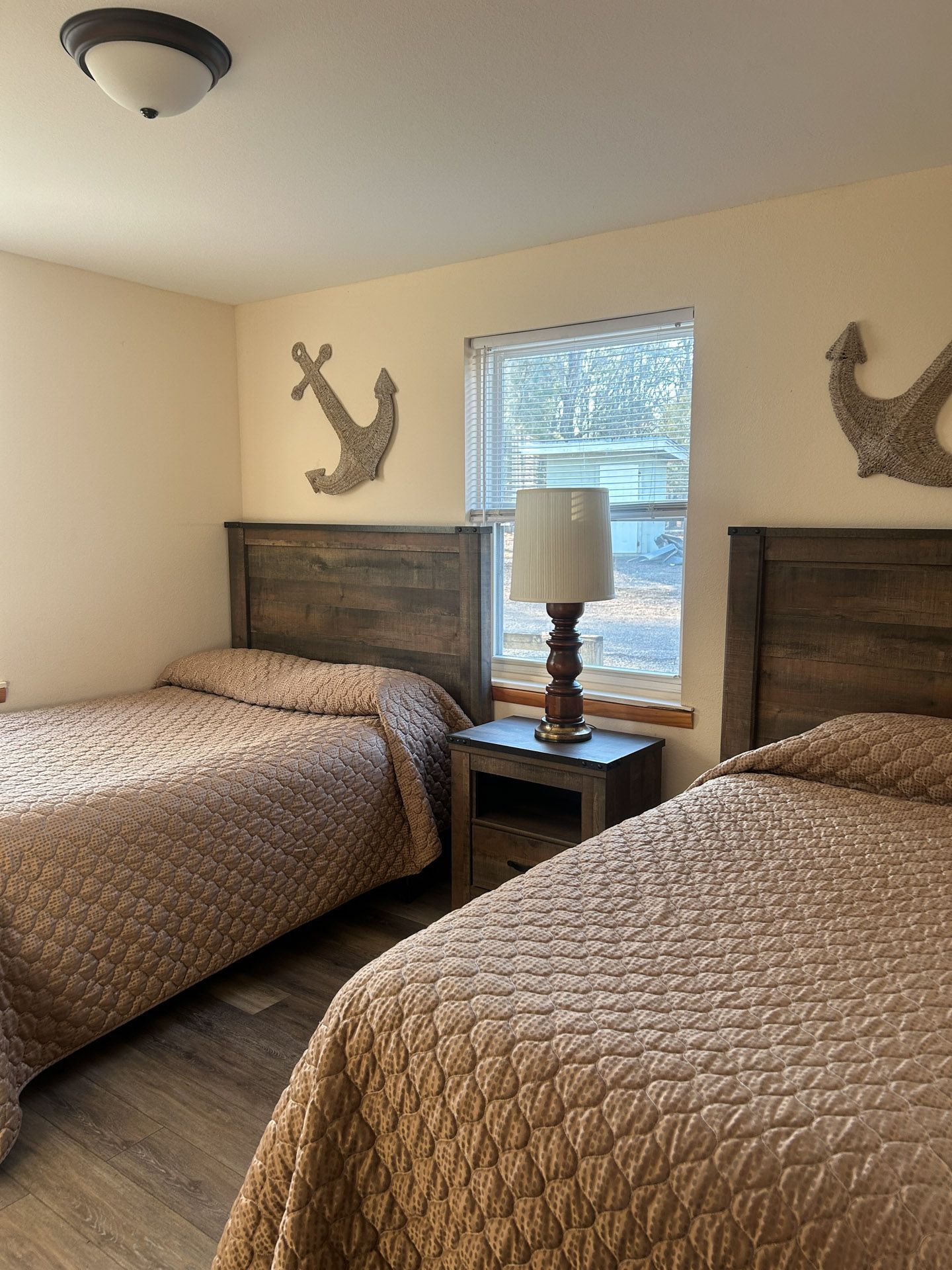 Bedroom with two twin beds, tan comforters, a nightstand with a lamp, and nautical decor on the walls.