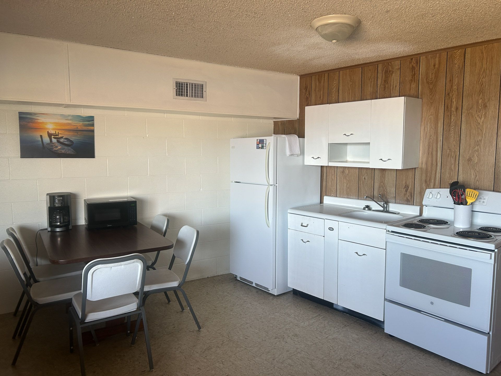 Kitchen with white appliances, wooden paneling, dining table, and four chairs.