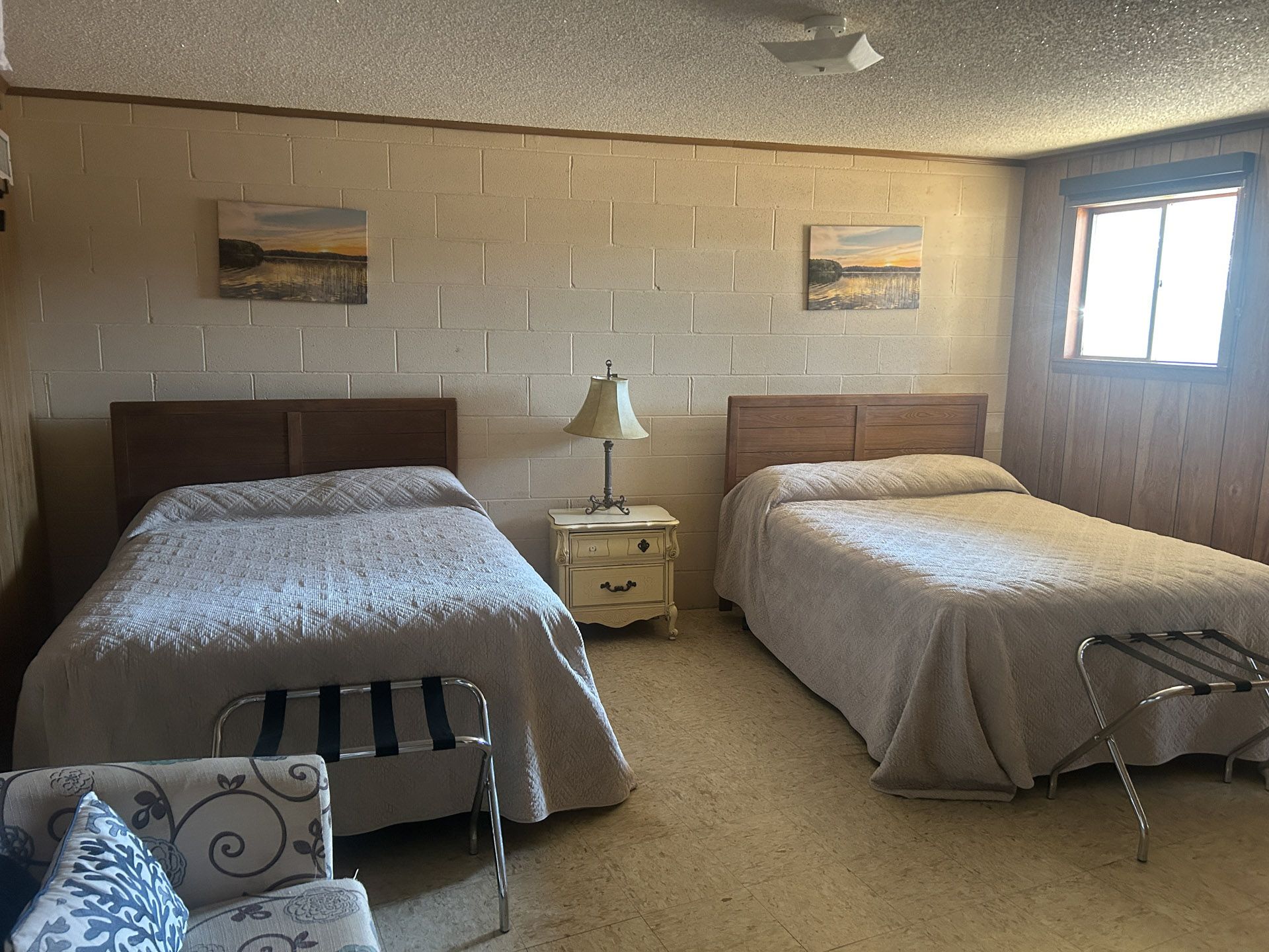 Two beds in a room with a nightstand, lamp, and two small paintings.