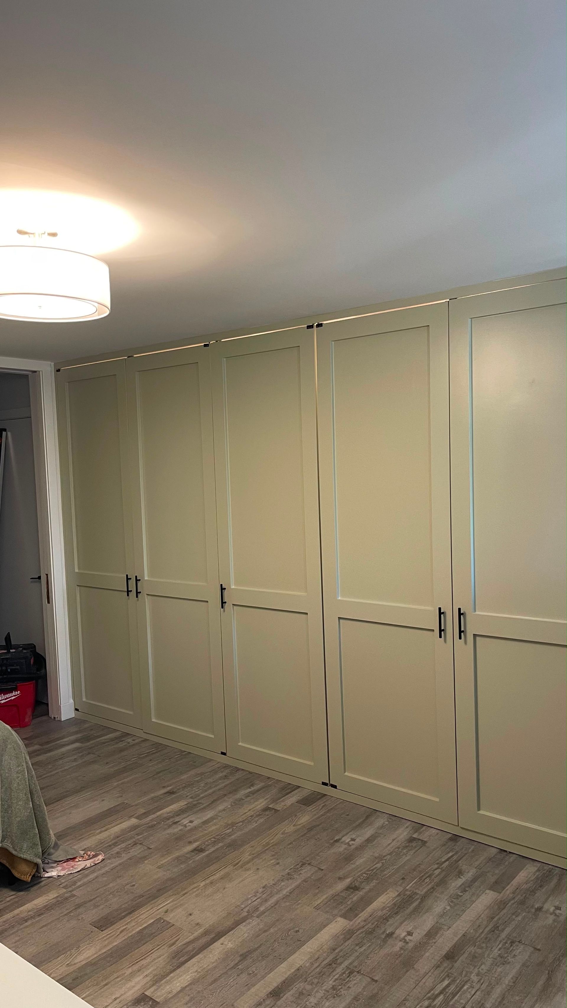 A room with beige built-in closets, gray wood flooring, and a ceiling light fixture.