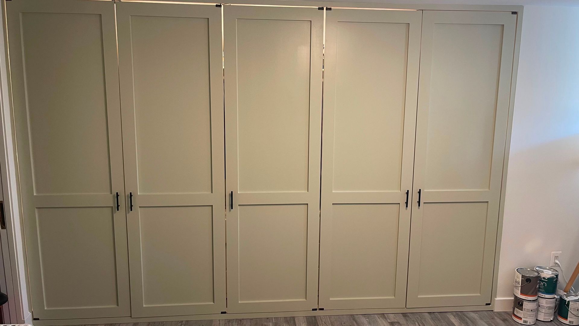 White built-in closet cabinets with paneled doors in a room; paint cans sit on the floor at right.