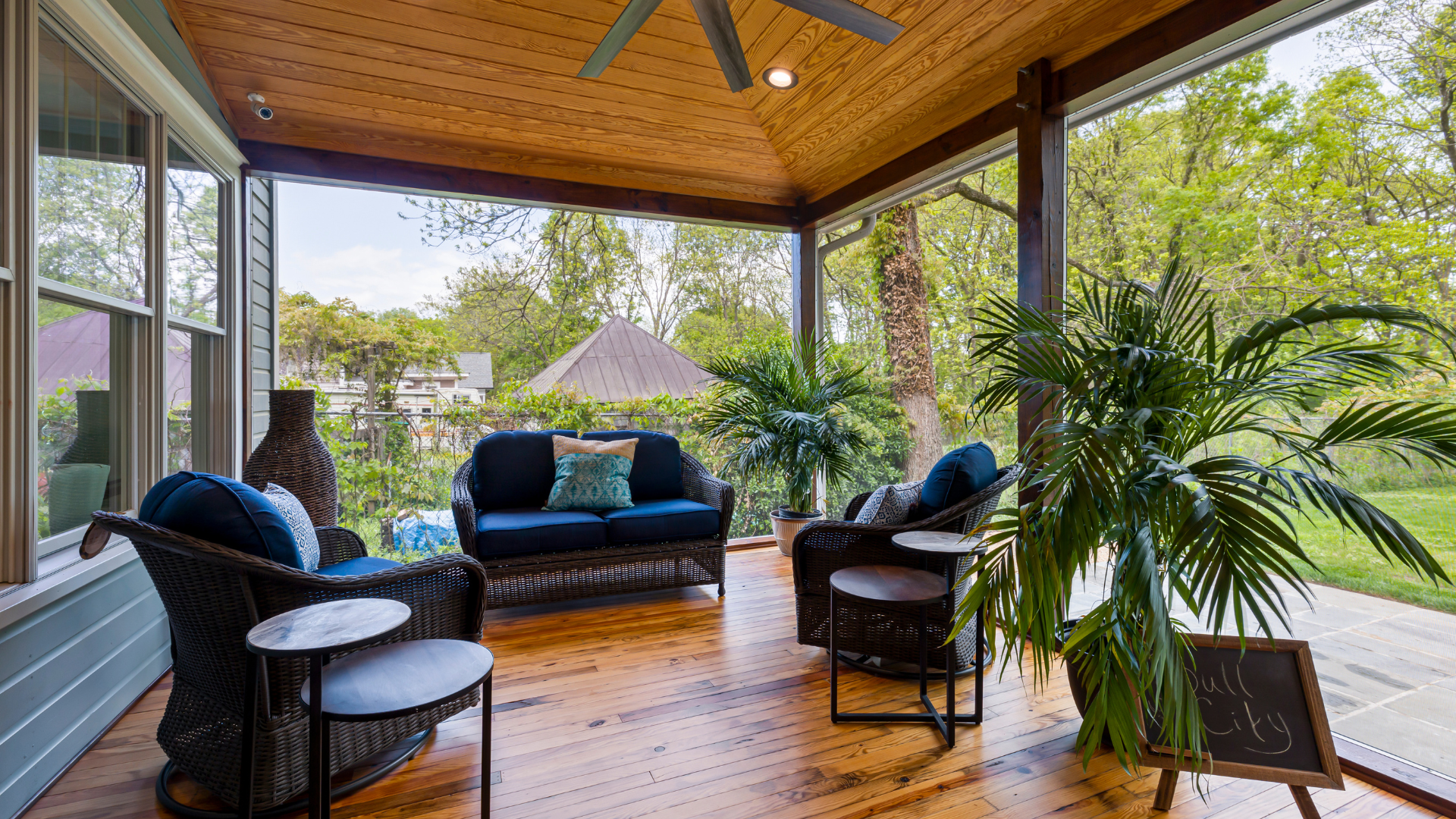 A screened in porch with a couch , chairs , tables and a ceiling fan.